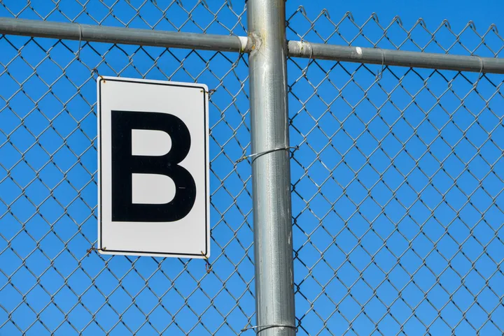 A sign marked B on a chain-link fence against a blue sky.